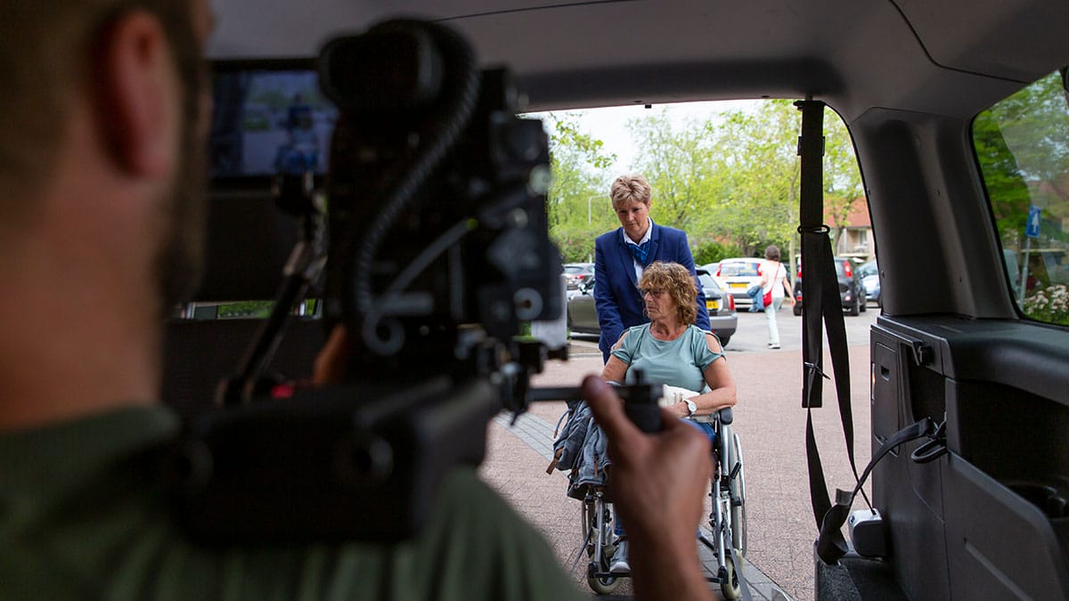 Kevin achterin de auto filmt een vrouw in een rolstoel die de auto in wordt geschoven