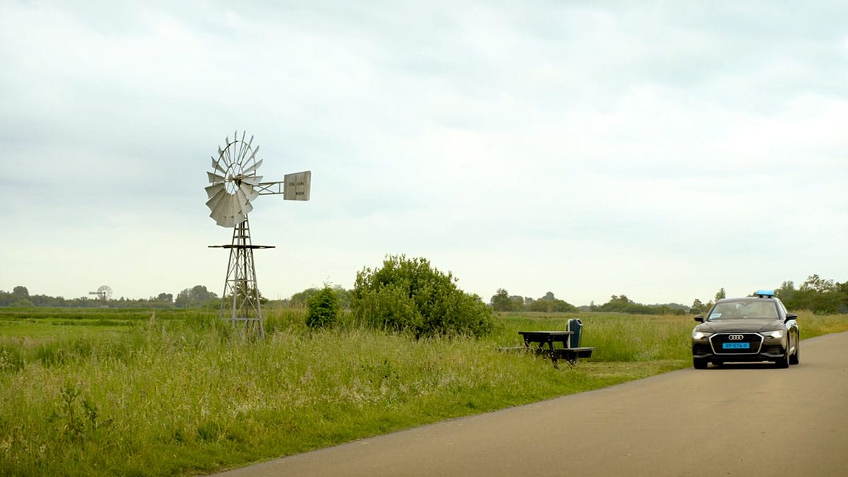 Een auto von Kijlstra rijdt langs een weg met een molentje